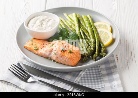 Filetto di salmone selvatico con asparagi servito con salsa tartara e primo piano al limone in un piatto sul tavolo. Orizzontale Foto Stock