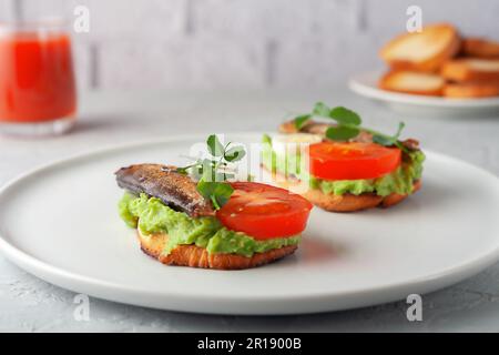 Sandwich con spratti su fette di pane tostate. Sandwich con spratto affumicato - pesce, avocado e pomodoro con uova. Foto Stock