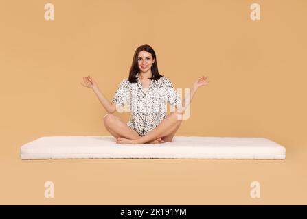 Giovane donna meditando su morbido materasso su sfondo beige Foto Stock