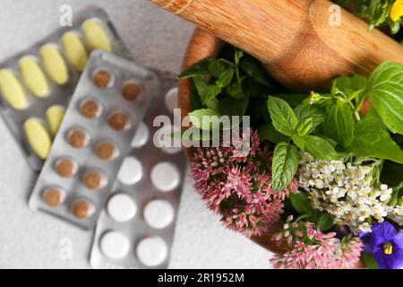 Mortaio di legno con erbe fresche, fiori e pillole su tavolo bianco, vista dall'alto Foto Stock