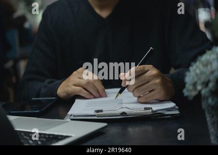 Persona aziendale con penna che firma documenti finanziari, approva lavoro, legge contrattuale o lavoro cartaceo sulla scrivania. Foto Stock