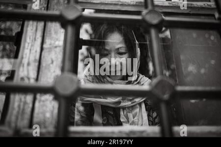 Una donna asiatica (vietnamita), che indossa un velo, dietro una finestra alla Moschea Suleymaniye del 16th ° secolo all'interno del castello di Alanya, Turchia, guarda in giù in c Foto Stock