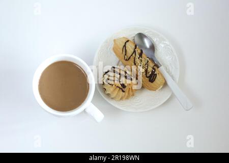 Eclairs su un piattino. Una tazza di caffè con latte. Su un piano portapaziente bianco. Preso dall'alto. Foto Stock