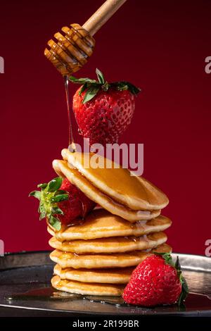 Levitating fragola su una pila di frittelle gocciolate con miele. Ripresa concettuale. Foto Stock