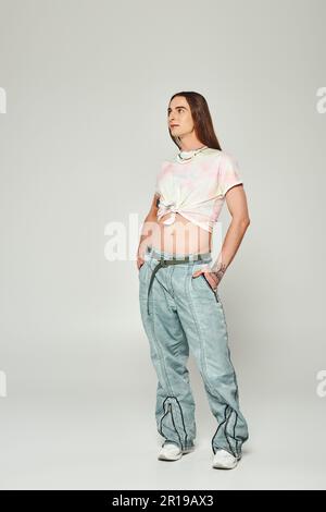 Tutta la lunghezza dell'uomo homosexual tatuato e a capelli lunghi che tiene le mani nelle tasche dei jeans del denim e che guarda via durante il celebratio di orgoglio della Comunità di lgbt Foto Stock