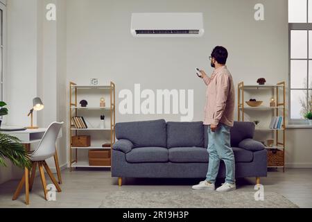 L'uomo usa il telecomando per accendere o regolare il condizionatore d'aria appeso nel suo ufficio di casa. Foto Stock