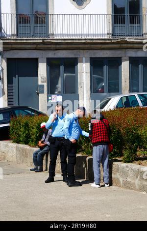 Polizia di pubblica sicurezza portoghese che controlla i documenti di una persona seduta nella piazza a vicino al centro della città, Porto / Porto, Portogallo Foto Stock