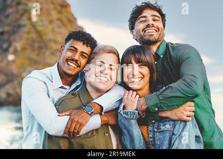 Ritratto di quattro amici multiculturali che si abbracciano e si propongono per una foto sul lungomare, con un individuo che si identifica come non binario, s Foto Stock
