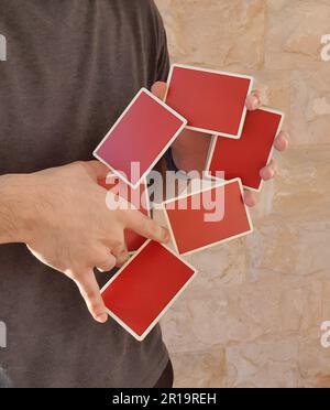 Un giovane che esegue un trucco di carta con un mazzo di carte rosse da gioco. Foto Stock