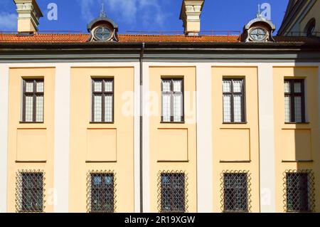 Splendidi edifici medievali europei di colore giallo con tetto in tegole rosse e finestre rettangolari con bar. Foto Stock