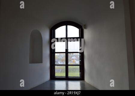 Una piccola finestra nera stretta con una cornice su una vecchia pietra bianca parete di cemento spesso in un vecchio castello. Lo sfondo. Foto Stock