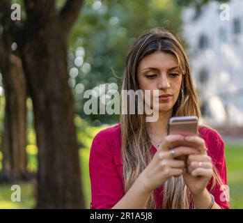 Ritratto di giovane donna bionda sorridente che cammina all'aperto e usa lo smartphone. Concetto di tecnologie moderne Foto Stock