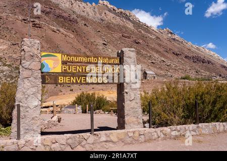 Cartello per il Monumento Naturale Puente del Inca nelle Ande dell'Argentina. La Cappella di nostra Signora delle Nevi è alle spalle. Foto Stock