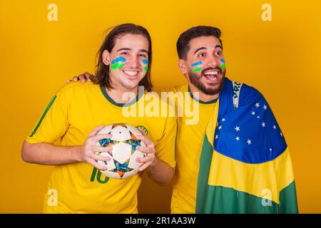 Amici brasiliani, latinoamericani, la diversità, il tifo per il brasile, nella Coppa del mondo 2022, tenendo la palla e la bandiera, attento al gioco, felice Foto Stock