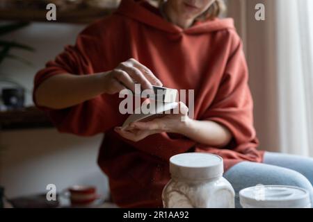 Primo piano mani ceramista donna con piattino e spugna dura per la lucidatura piatti dopo forno di ceramica Foto Stock