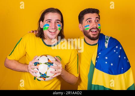 Amici brasiliani, latinoamericani, la diversità, il tifo per il brasile, nella Coppa del mondo 2022, tenendo la palla e la bandiera, attento al gioco, felice Foto Stock