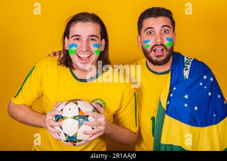 Amici brasiliani, latinoamericani, la diversità, il tifo per il brasile, nella Coppa del mondo 2022, tenendo la palla e la bandiera, attento al gioco, felice Foto Stock