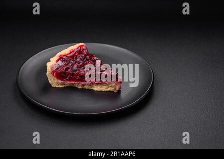 Deliziosa torta dolce profumata con ciliegie su un piatto di ceramica su fondo di cemento scuro Foto Stock