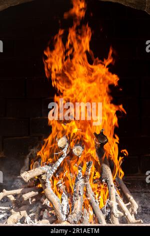 Un falò alto con linguette affilate di fiamme gialle e arancioni su uno sfondo di fumo scuro in muratura. Un forno per barbecue all'aperto. Preparazione di Foto Stock