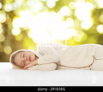 Bambina che dorme su un comodo materasso su sfondo verde sfocato, effetto bokeh. Dormi bene - resta in salute Foto Stock