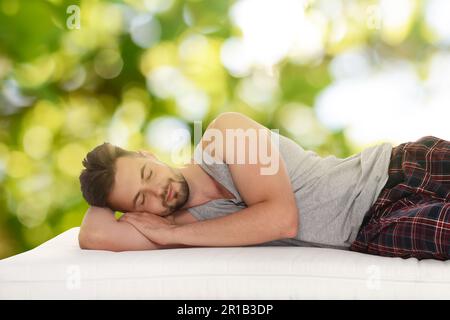 Uomo che dorme su un comodo materasso su sfondo verde sfocato, effetto bokeh. Dormi bene - resta in salute Foto Stock