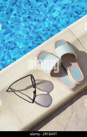 Occhiali da sole e ciabatte eleganti a bordo piscina nelle giornate di sole. Accessori da spiaggia Foto Stock