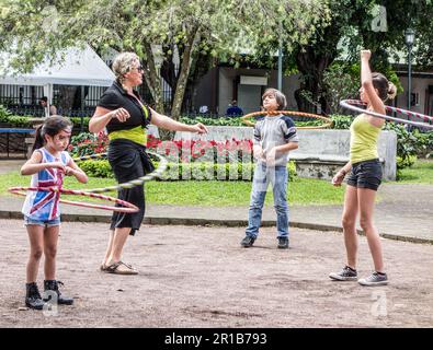 Donna adulta che gioca con cerchi di lula con tre bambini in un parco a San José, Costa Rica. Foto Stock