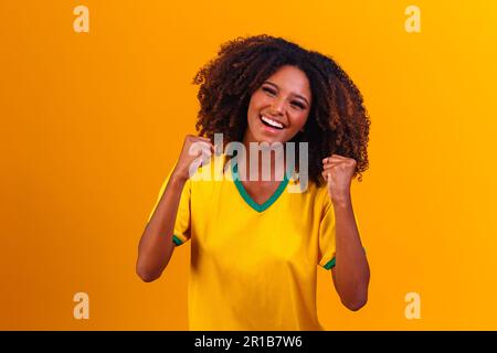 Sostenitore brasiliano. Tifoso brasiliano che festeggia sul calcio o sulla partita di calcio su sfondo giallo. Colori del Brasile. Foto Stock