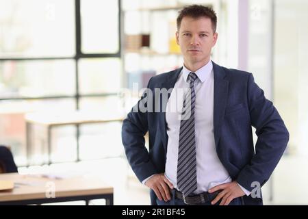 Il serio uomo d'affari tiene le mani sui fianchi in piedi in ufficio Foto Stock