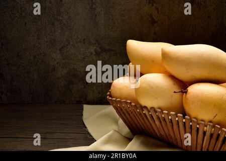 Mango thailandesi in cesti di vimini su tavolo di legno e sfondo scuro.Horizontal.Copy space.Copy text.Yellow mango in cesti.mango nam dok mai. Foto Stock