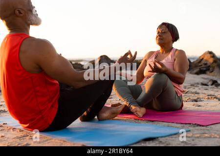 Felice coppia afroamericana che pratica yoga su materassini yoga e meditare in spiaggia Foto Stock