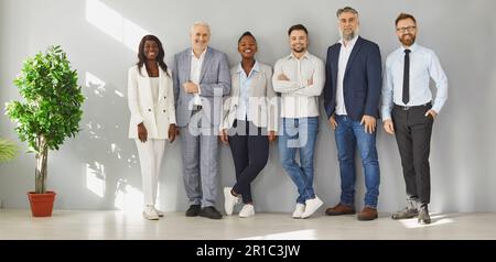 Uomini d'affari multiculturali felici in fila contro il muro in ufficio Foto Stock