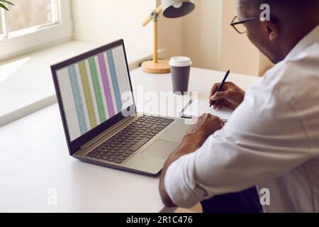 Vista laterale di un giovane uomo d'affari che lavora su un computer portatile con tavoli in ufficio e scritture. Foto Stock