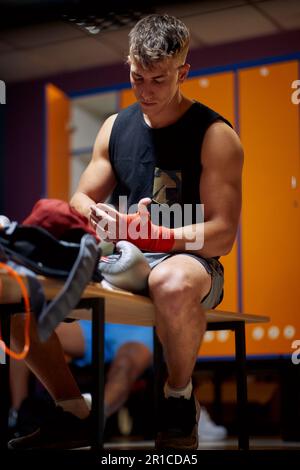 Bel giovane uomo messo a fuoco legando nastro rosso intorno alle sue mani preparandosi per l'allenamento di boxe. Arti marziali, salute, concetto di stile di vita. Foto Stock