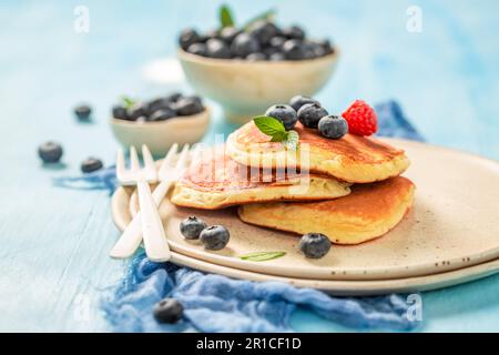 Dolci e gustosi pancake americani con mirtilli e lamponi. Frittelle dolci per colazione su un tavolo blu. Foto Stock