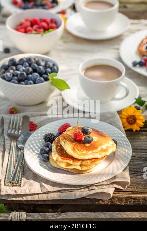 Deliziosi pancake americani fatti in casa con lamponi, miele e mirtilli. Prima colazione nel giardino primaverile. Foto Stock