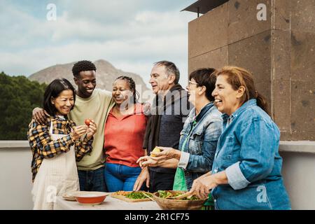 Amici multi generazionali che hanno divertimento cucinando insieme sul tetto della casa - incontri estivi e concetto di cibo Foto Stock