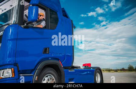 Conducente semi-camion caucasico in attesa di un rimorchio con carico di spedizione. Tema dei camionisti. Parcheggio. Foto Stock