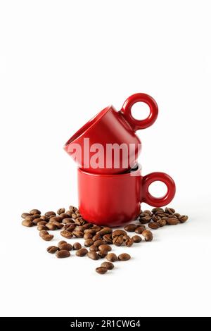 Due tazze da caffè impilate con chicchi di caffè sparsi su sfondo bianco Foto Stock