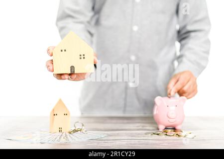 Uomo d'affari che tiene simulata casa di legno sullo sfondo bianco sfocato in ufficio con uno spazio copia lato sinistro. Il concetto per budg immobiliare Foto Stock