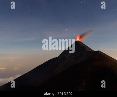 Vulcano fuego eruzione lava di notte con stelle visibili e luci della città ad Antigua, Guatemala Foto Stock