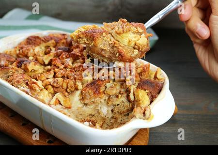 A mano con cucchiaino di pappetitoso pane alla noce di banana Pudding da ciotola in ceramica su tavolo in legno Foto Stock