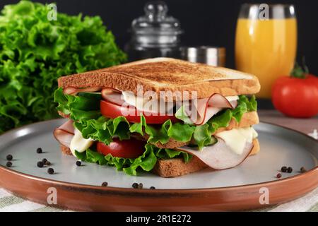 Delizioso sandwich al prosciutto con insalata fresca e pomodori serviti sul piatto. Foto Stock