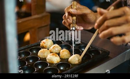 Un maschio che controlla le mini prelibatezze fritte assortite spiedate su bastoni di legno, stalla takoyaki Foto Stock