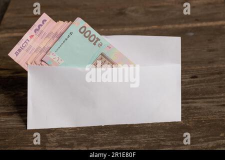 La valuta Ucraina si trova in una busta bianca su un tavolo di legno, stipendio in una busta Foto Stock