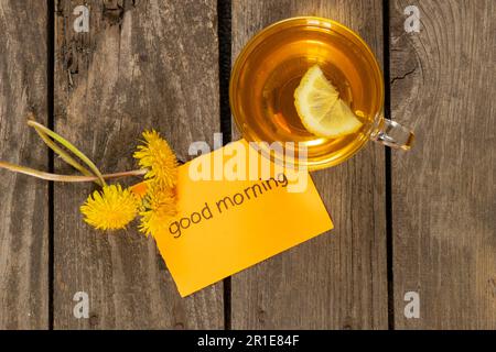 Una tazza di tè con dente di limone e le parole in inglese buon mattino Foto Stock