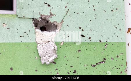 Buchi da proiettili e shrapnel nella parete sulla linea anteriore. Cicatrici di guerra. Muro di cemento di un edificio residenziale con buche e buchi da gunf Foto Stock