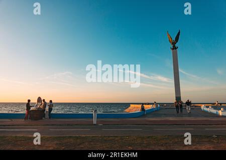 I residenti si rilassano lungo la malecón di fronte alla scultura dell'Angelo Maya a Campeche, Messico, al tramonto Foto Stock