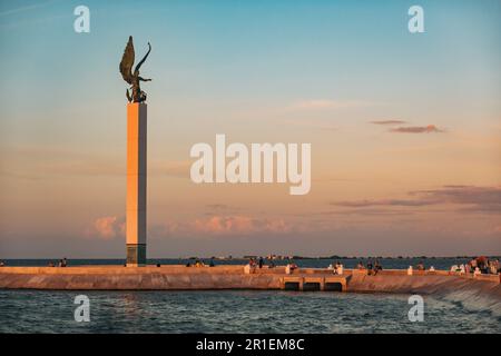 I residenti si rilassano lungo la malecón di fronte alla scultura dell'Angelo Maya a Campeche, Messico, al tramonto Foto Stock