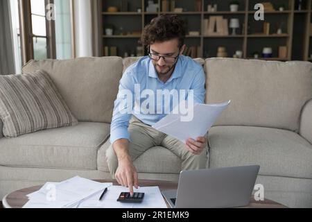 Un giovane imprenditore impegnato e focalizzato che usa la calcolatrice a casa Foto Stock